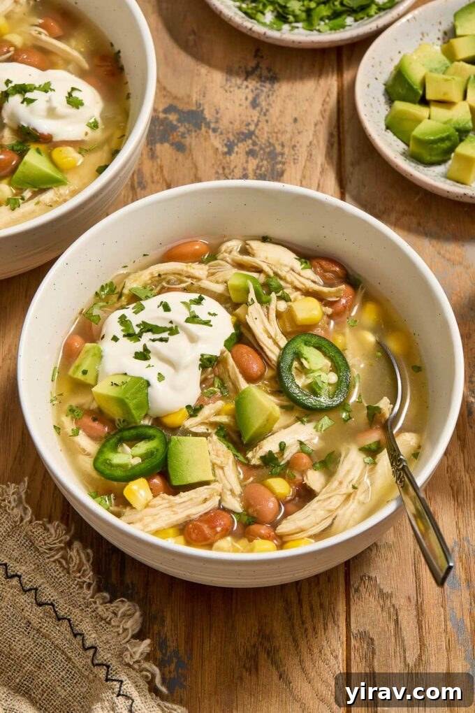 Bowl of green enchilada chicken soup with sour cream, avocado and jalapenos.