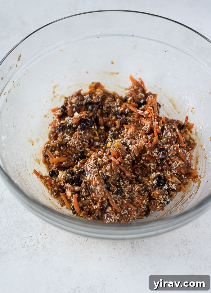Golden Spiced Carrot Oat Cookies 5 Grated carrots, shredded coconut, chopped walnuts, and raisins being stirred into the wet cookie ingredients.