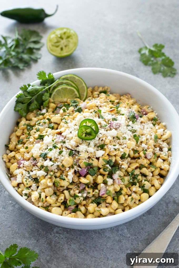 Vibrant Mexican corn salad served in a white bowl, garnished with fresh cilantro and a sliced jalapeño