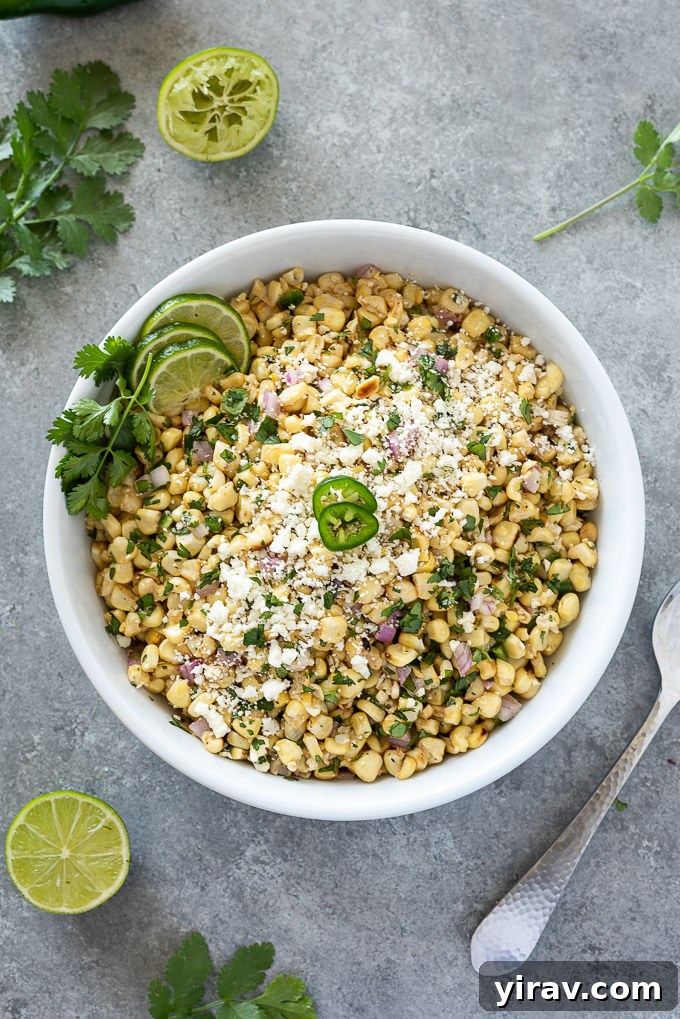 Close-up of Mexican corn salad in a pristine white bowl, garnished with fresh lime wedges and cilantro sprigs