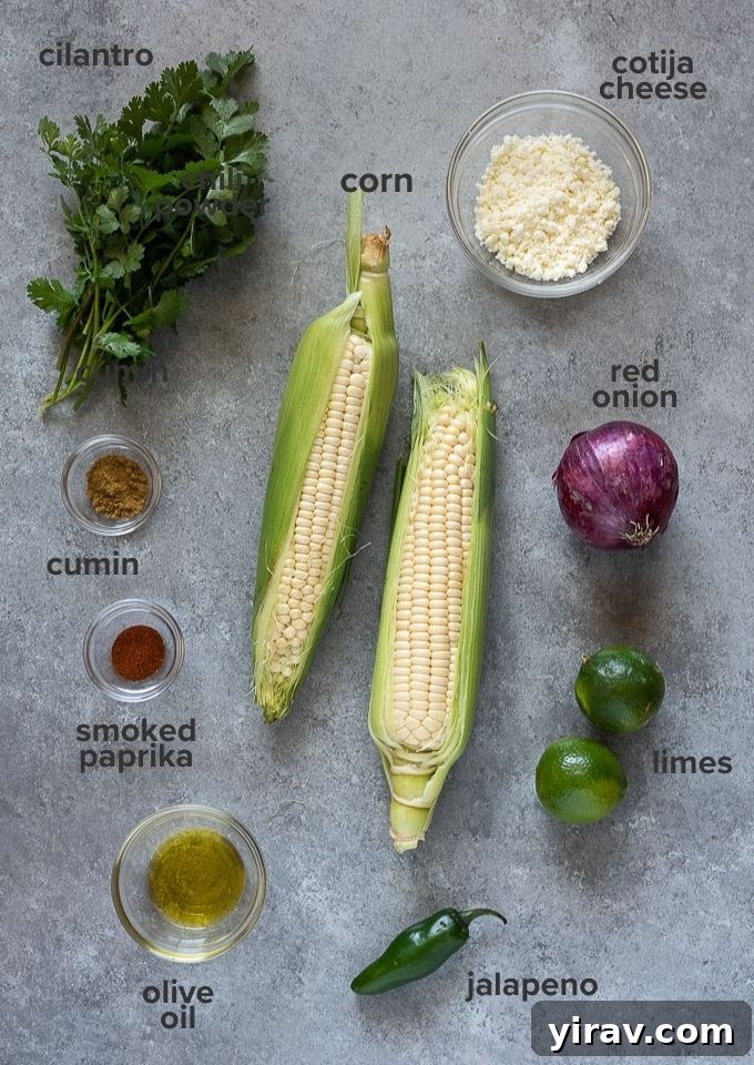 A flat lay photograph showcasing all the fresh ingredients needed for Mexican corn salad: ears of corn, lime, cilantro, red onion, jalapeño, and cotija cheese
