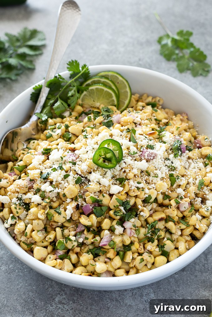 Grilled Mexican corn salad topped with fresh jalapeño slices, lime wedges, and cilantro sprigs in a serving bowl