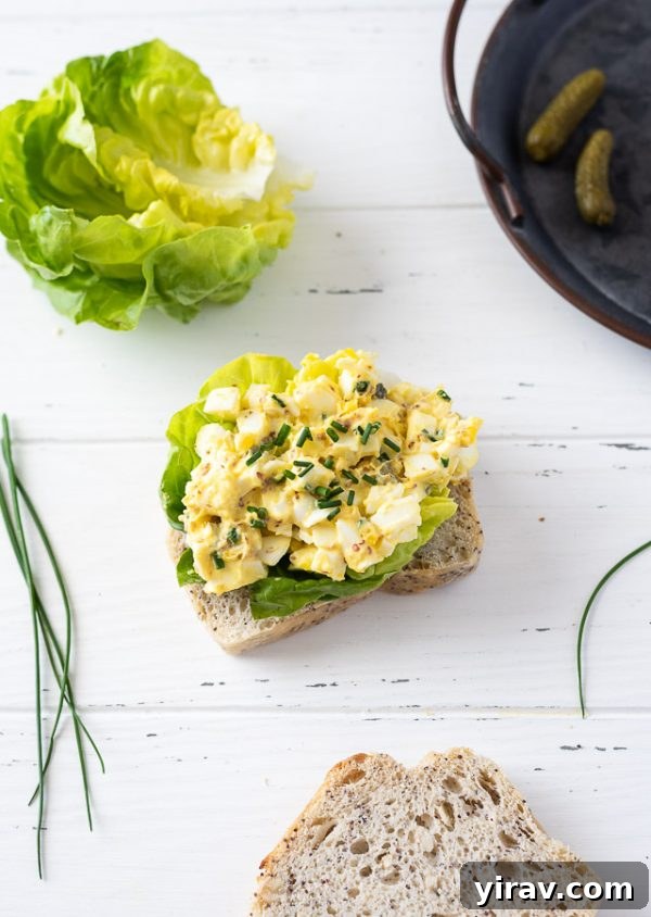Open-faced egg salad sandwich generously topped with fresh chives on a rustic wooden board