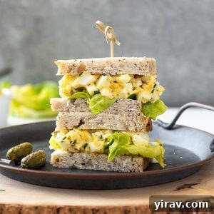 Creamy egg salad sandwich piled on a plate with a wooden pick