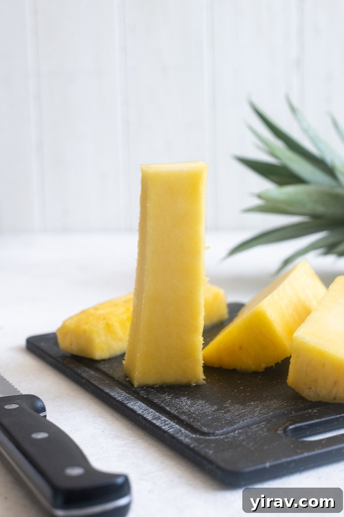 Quick & Creamy Pina Colada Dream 6 Pineapple core standing on a cutting board, with the cut pineapple flesh alongside.