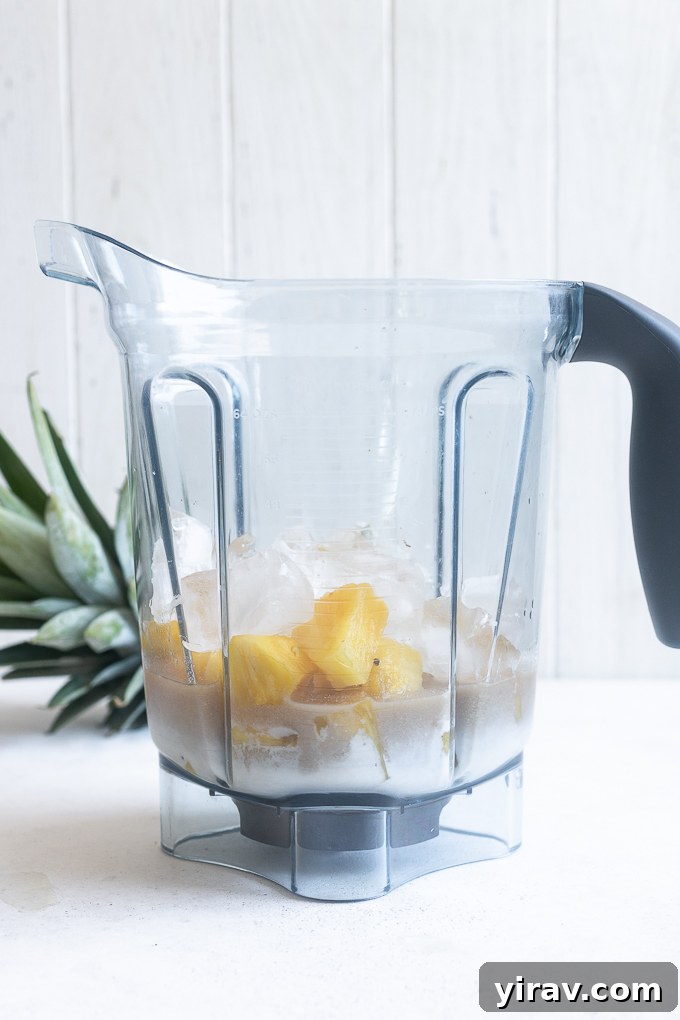 Quick & Creamy Pina Colada Dream 8 All pina colada recipe ingredients, including pineapple, coconut cream, rum, and ice, placed in a blender.