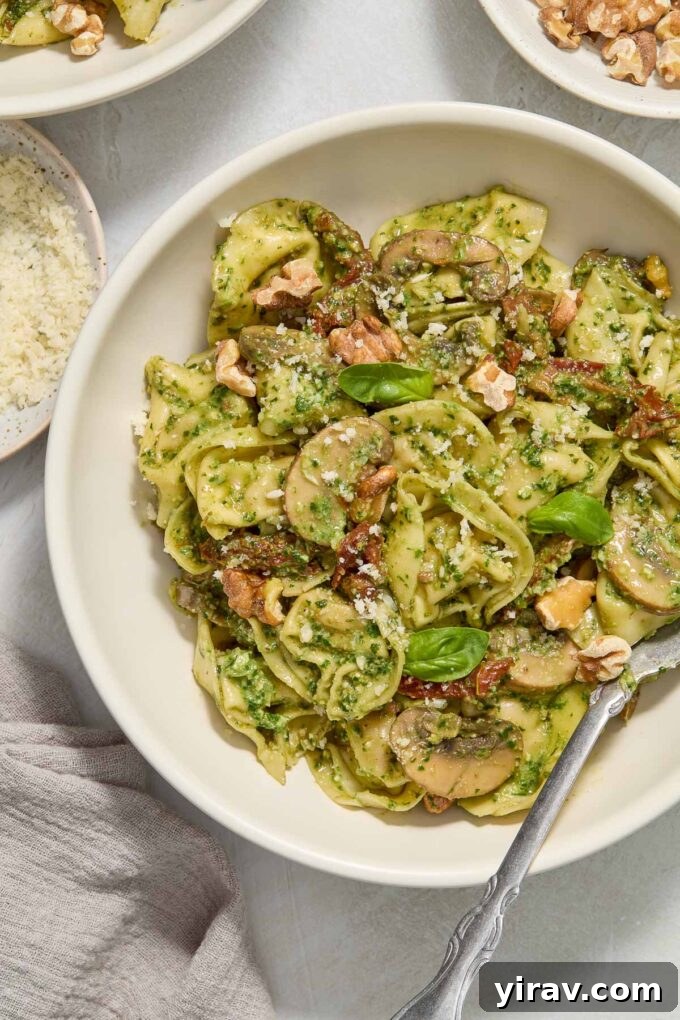 A close-up shot of creamy pesto tortellini served in a rustic bowl, with a fork dipping into the rich sauce and pasta, highlighted by fresh basil leaves.