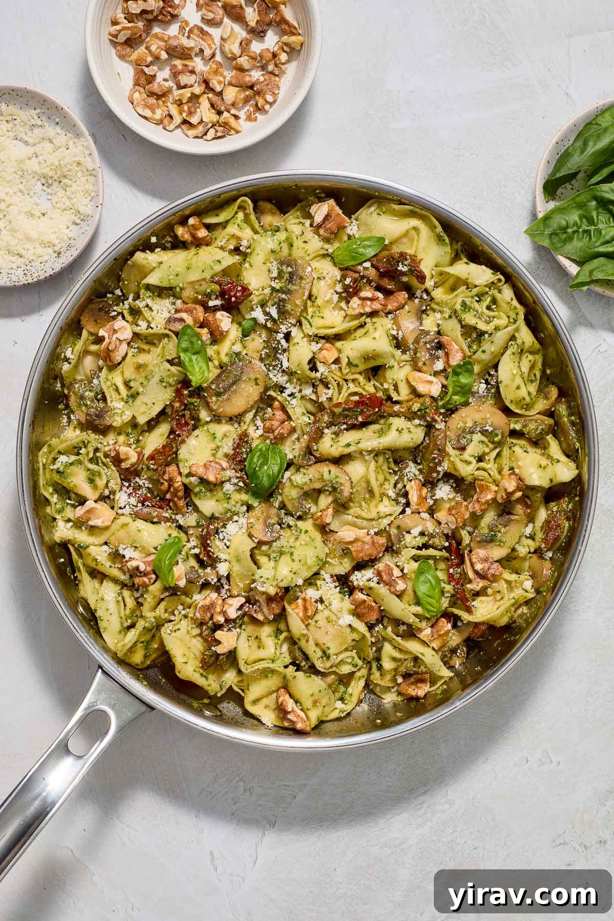 A vibrant close-up of creamy pesto tortellini simmering in a large skillet, garnished with fresh basil leaves, ready to be served.