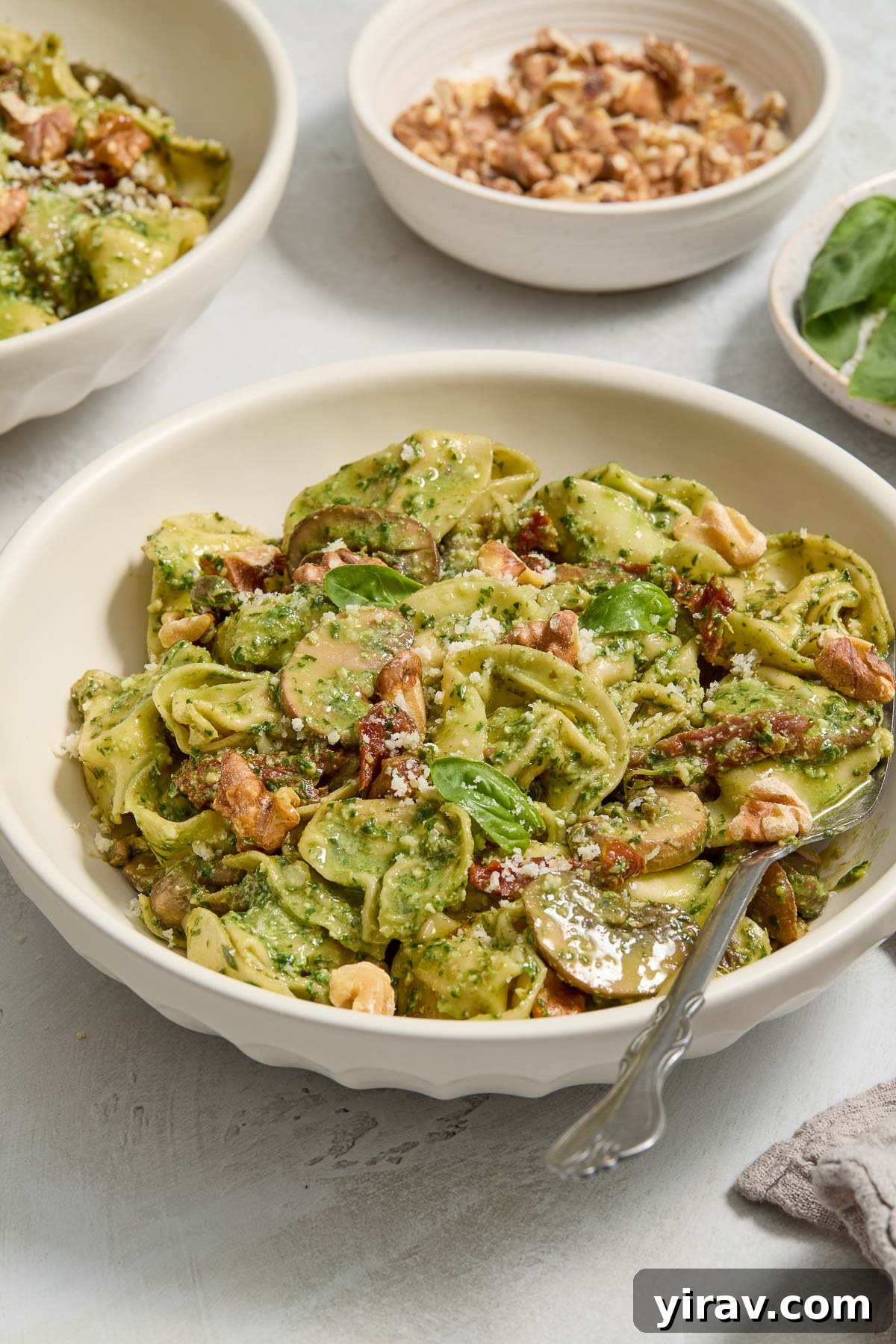 A bowl of creamy pesto tortellini, generously garnished with fresh basil leaves and toasted walnuts, ready to be enjoyed.