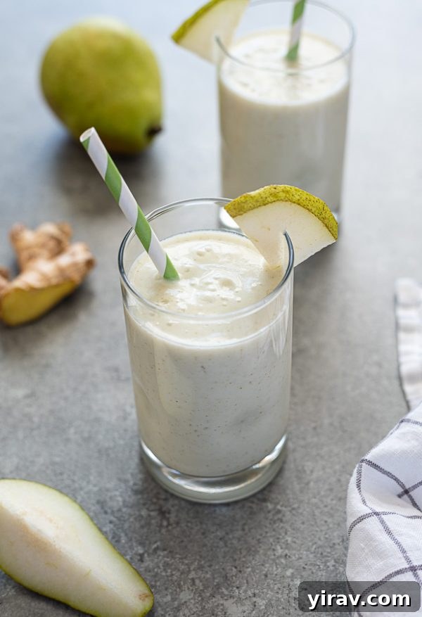 Front view of a pear ginger smoothie in a glass with a green striped straw, with fresh ginger root visible in the soft background, highlighting the key ingredients.