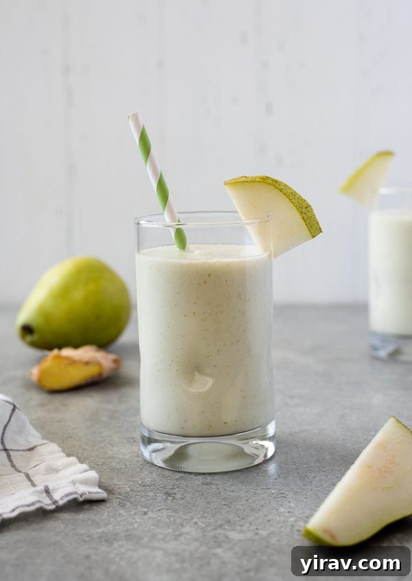 Close-up of a pear ginger smoothie, showcasing its creamy texture, with blurred fresh pear slices and ginger in the background, emphasizing natural ingredients.