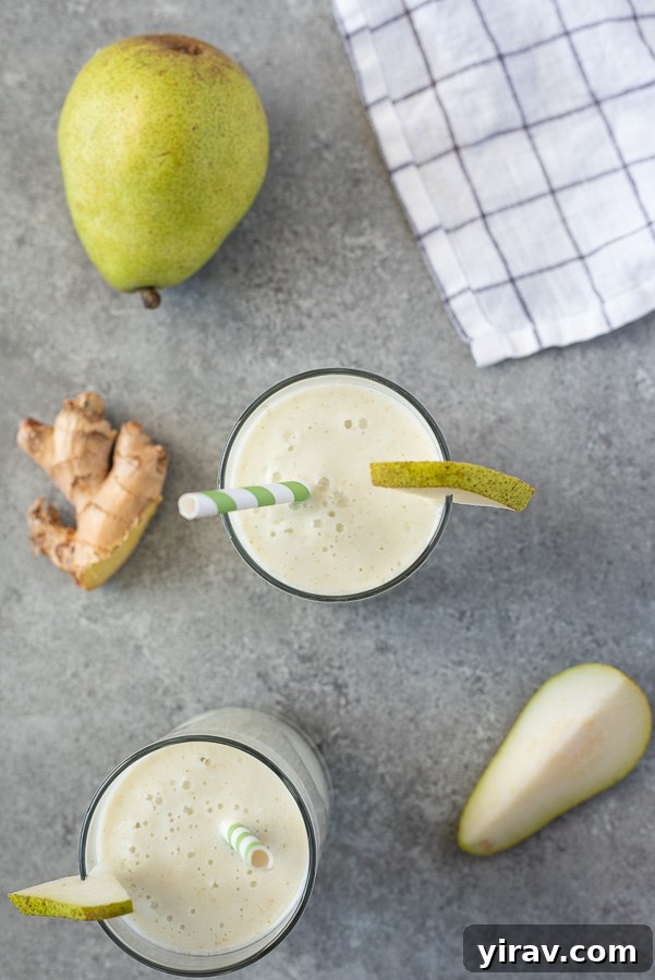 Overhead shot of a pear ginger smoothie in a glass with a straw and a slice of fresh pear, ready to be enjoyed.