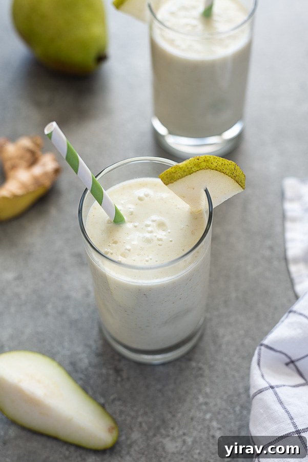 Angled overhead shot of a pear ginger smoothie in a glass with a green striped straw, showcasing its appealing texture and presentation.