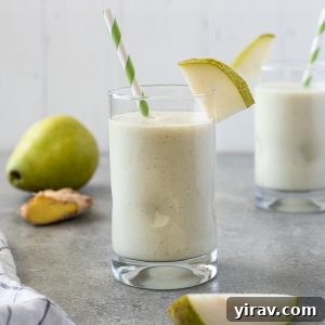 Pear smoothie in glass with striped straw and slice of pear
