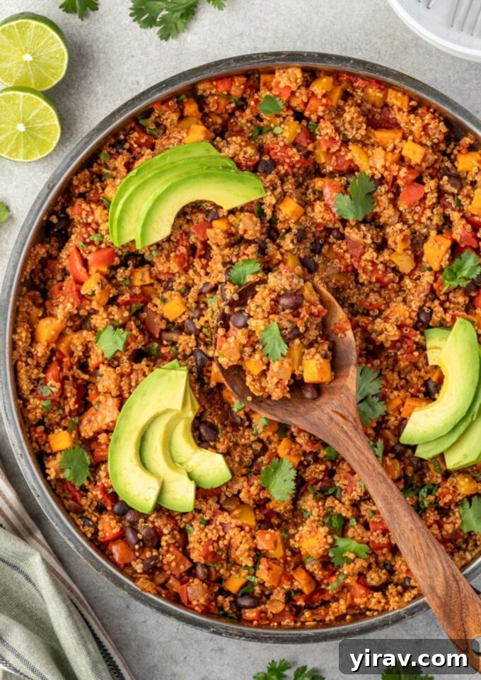 Vibrant Mexican quinoa in a pan with a wooden spoon, garnished with fresh cilantro and avocado slices