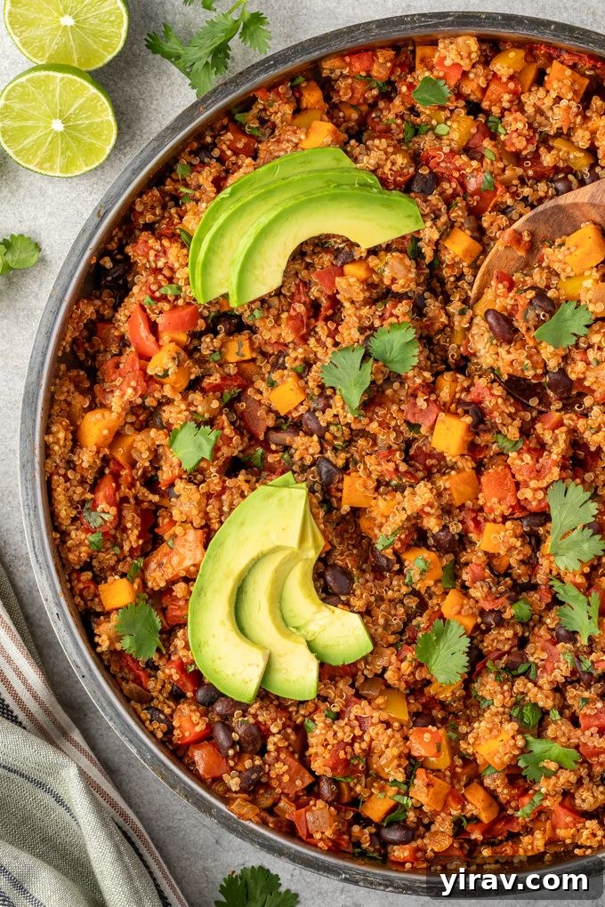 Mexican quinoa simmering in a skillet, topped with fresh avocado slices and cilantro