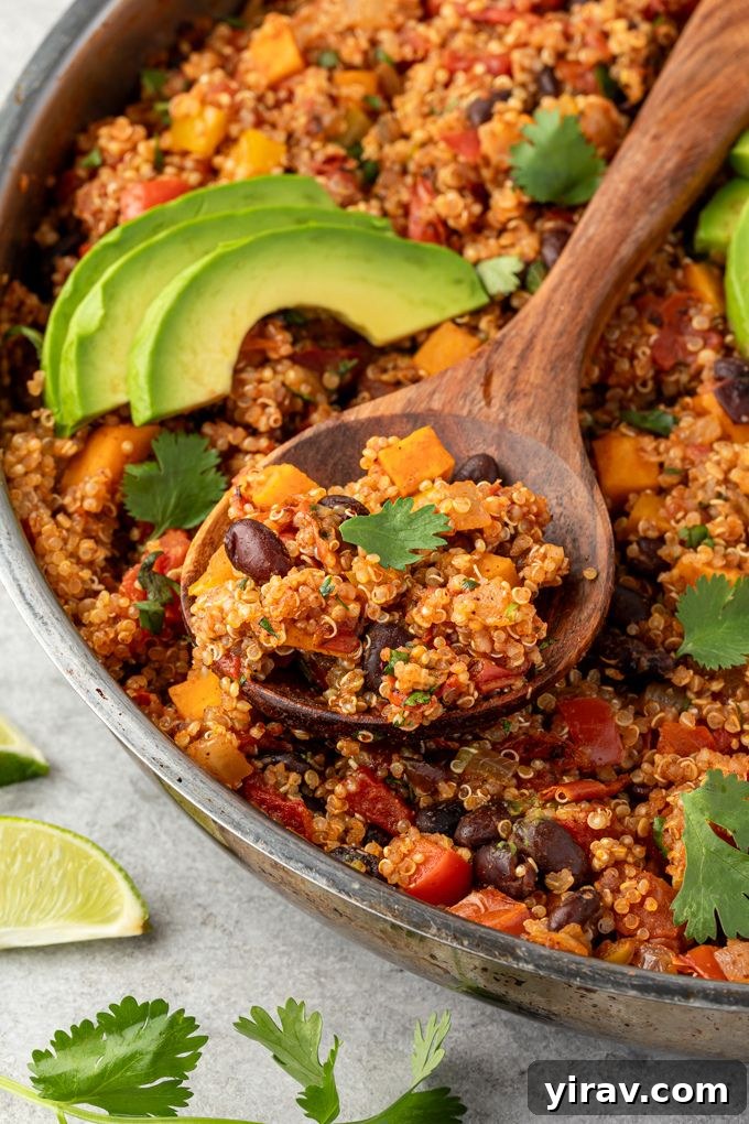 A wooden spoonful of Mexican quinoa, adorned with fresh cilantro and a slice of avocado, held over the pan