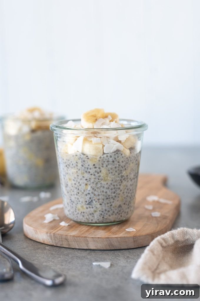 A jar of healthy and creamy banana chia pudding topped with fresh banana slices and a sprinkle of coconut flakes, presented on a rustic cutting board.