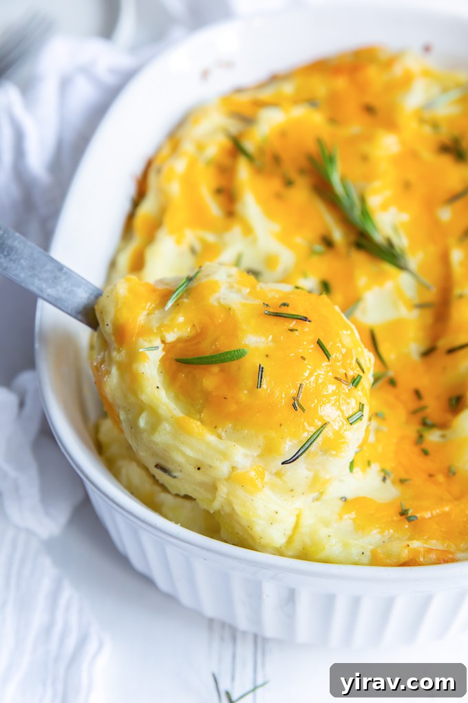 A serving spoon digging into the creamy, cheesy twice baked mashed potatoes, showcasing its texture.