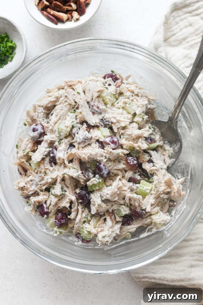 Chicken salad with grapes being mixed in a clear glass bowl, showcasing its fresh ingredients.
