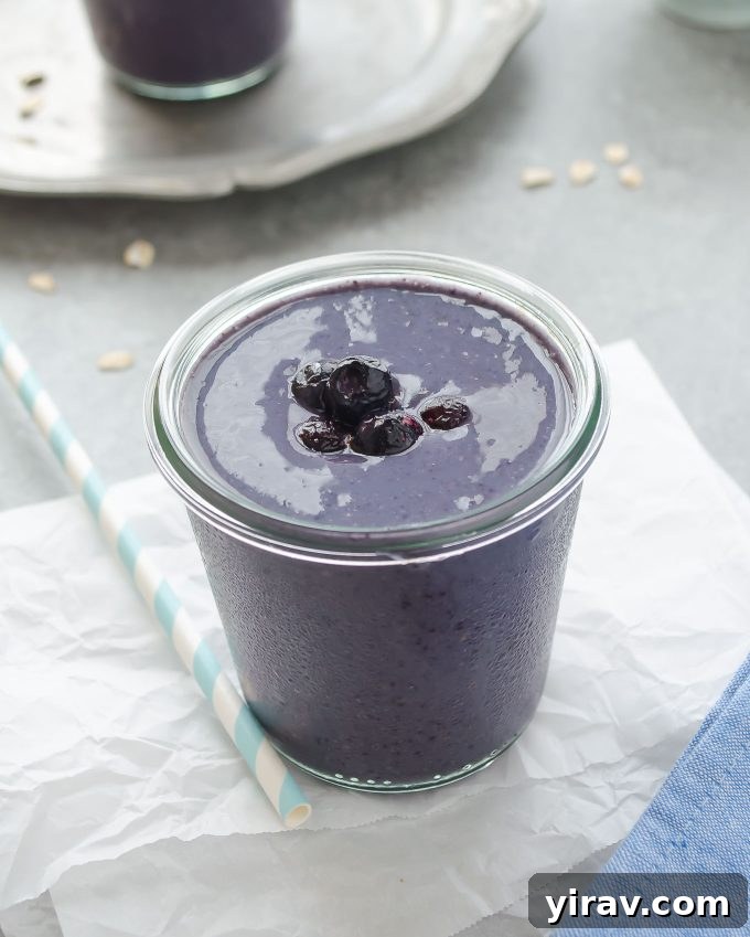 Creamy blueberry banana oat smoothie in a clear glass, garnished with fresh blueberries and a sprinkle of oats, ready to be enjoyed.