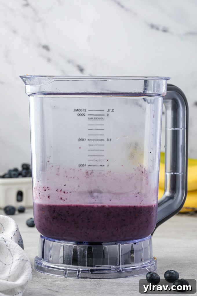 A high-angle shot of a blender filled with fresh and frozen ingredients for a blueberry banana smoothie, ready for blending.