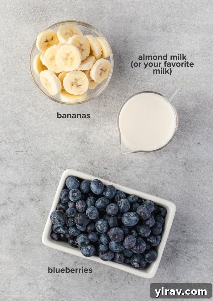 A vibrant flat lay of individual ingredients required for a blueberry banana smoothie, including fresh blueberries, ripe bananas, a carton of almond milk, and a portion of oats.