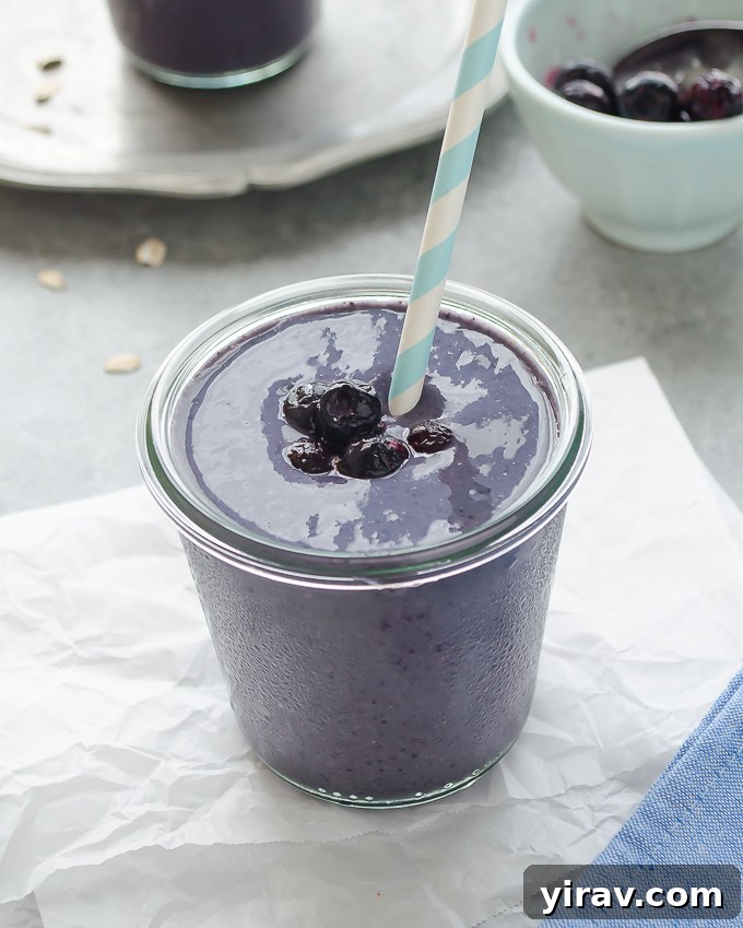 A refreshing blueberry banana oat smoothie in a stylish glass jar with a straw, garnished with fresh blueberries, presented on a bright background.