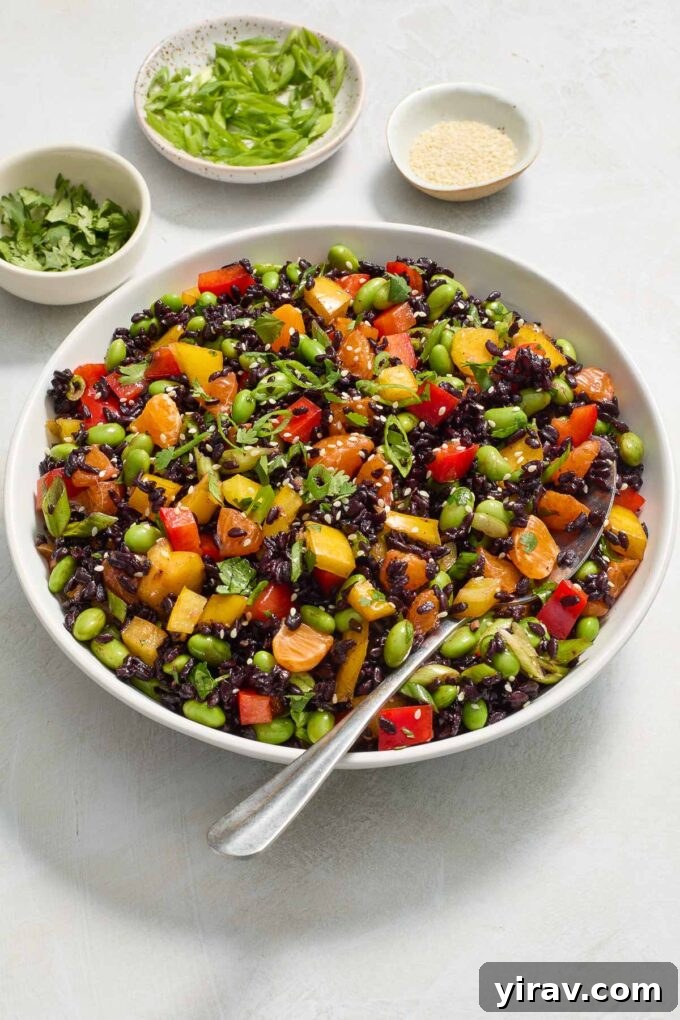 Asian black rice salad in a bowl with a serving spoon, garnished with sesame seeds.