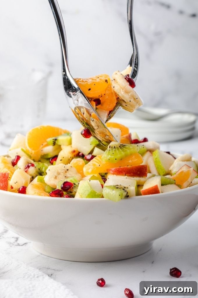 Serving spoons gently tossing colorful winter fruit salad in a white bowl