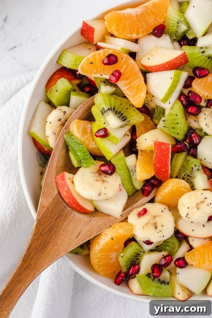 A wooden spoon scooping into a bowl of vibrant winter fruit salad