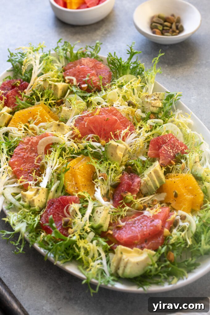 A vibrant Citrus Frisée Salad on a platter, garnished with creamy avocado and crunchy pistachios.