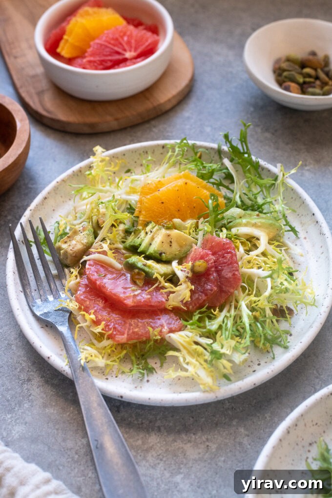 A beautifully arranged frisée salad with citrus, avocado, and pistachios on a white plate, ready to be enjoyed.