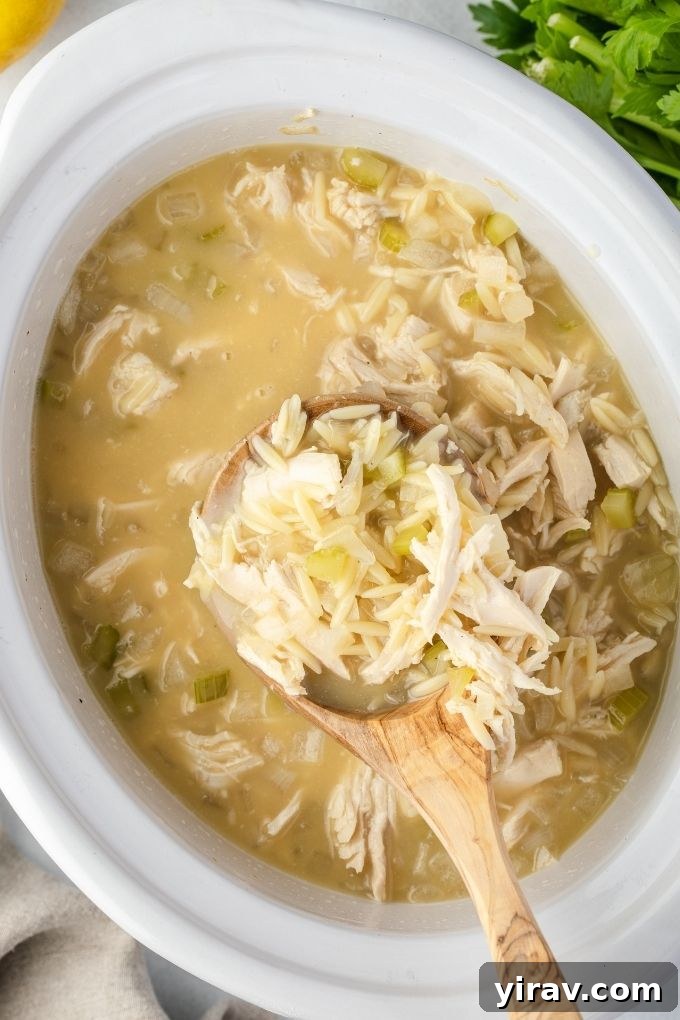 A spoonful of creamy avgolemono soup being lifted from a slow cooker, showcasing the shredded chicken and rice within.