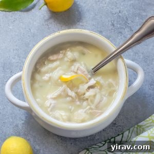 Slow cooker Greek lemon chicken soup in a white bowl, garnished with fresh dill and a lemon slice.