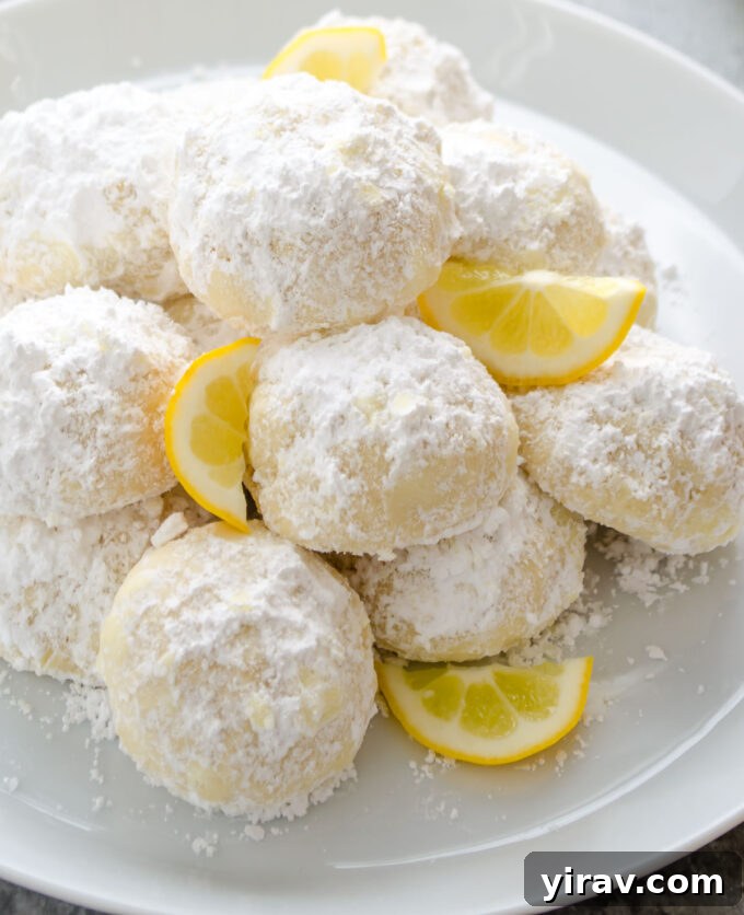 Kourabiedes piled on a plate with slices of lemon.