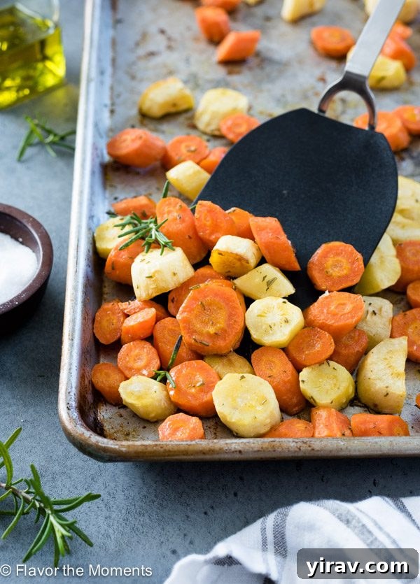 A baking sheet filled with perfectly roasted carrots and parsnips, glistening and golden-brown, with a spatula.