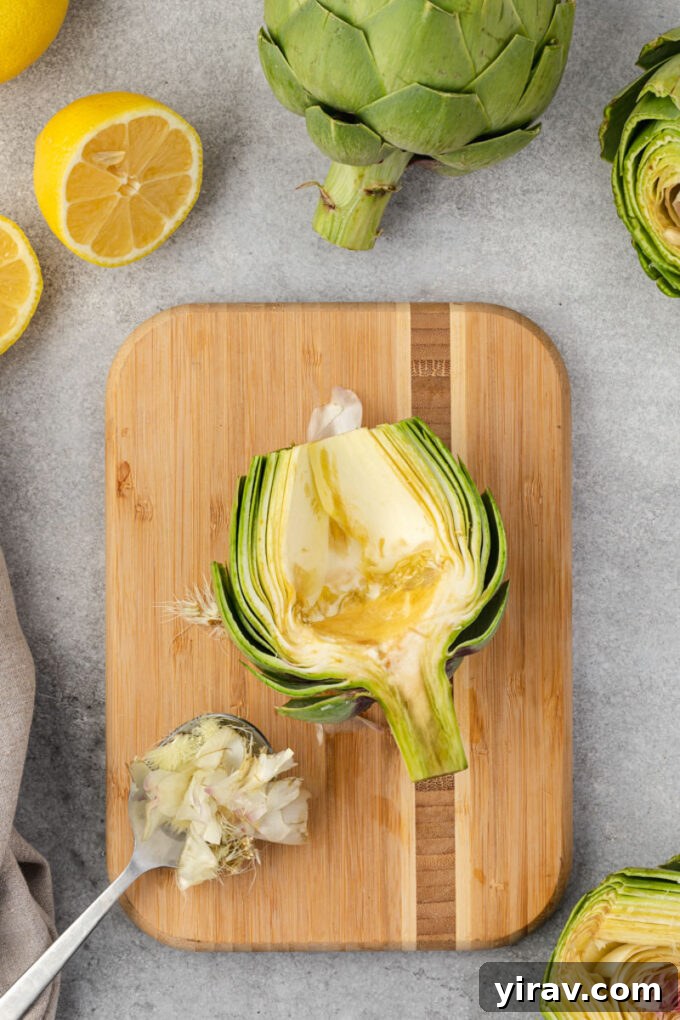 Using a spoon to scoop out the fuzzy choke from the center of a halved artichoke.