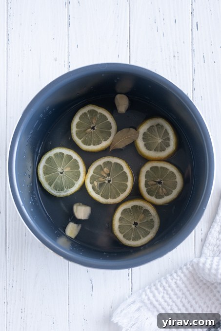 Water with lemon slices, garlic and bay leaf in bottom of Instant Pot.