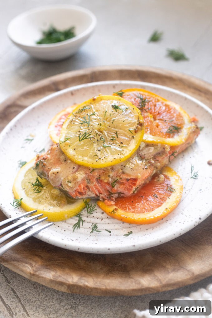 Citrus salmon on a plate with lemon and orange slices and chopped fresh dill.