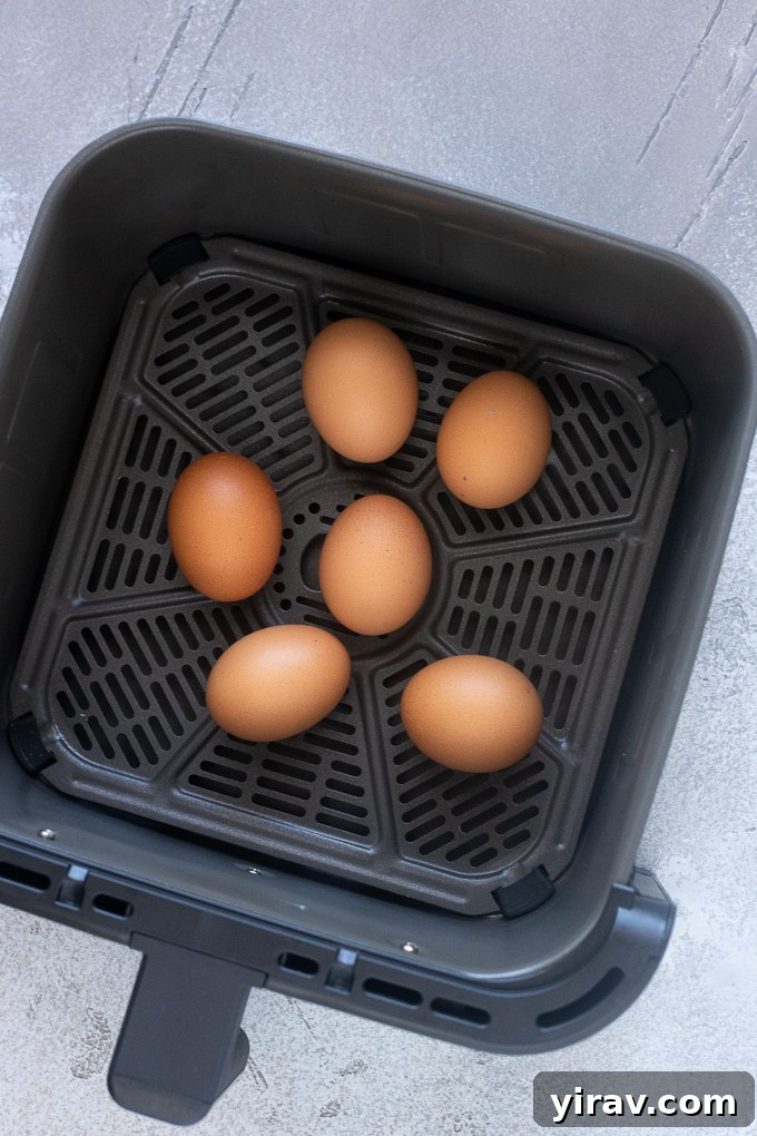 Hard boiled eggs being carefully placed into the air fryer basket for cooking.