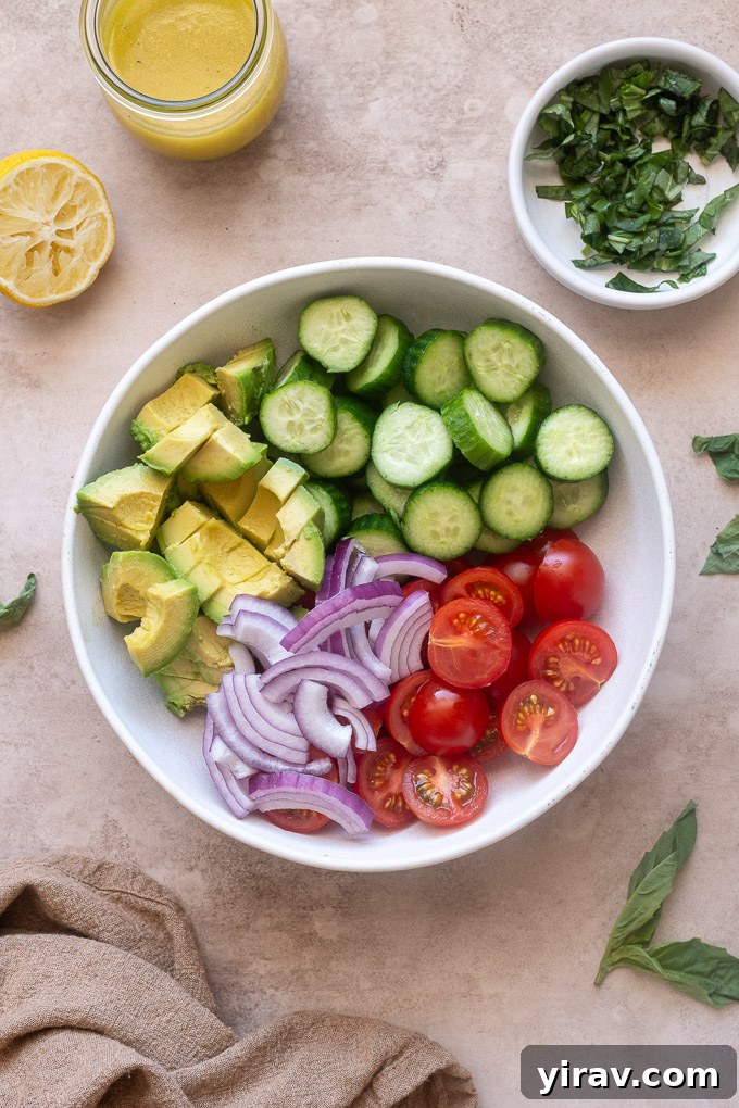 Chopped cucumbers tomatoes avocado unmixed in a bowl.