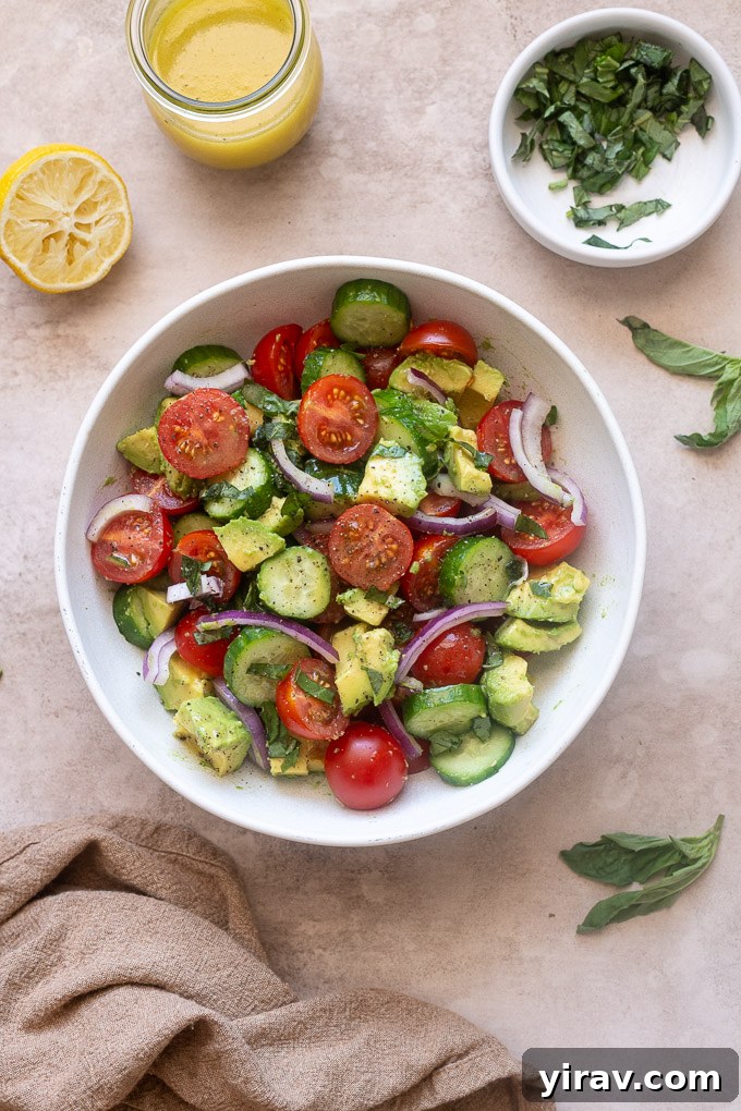 Cucumber tomato avocado salad in a bowl with fresh basil.