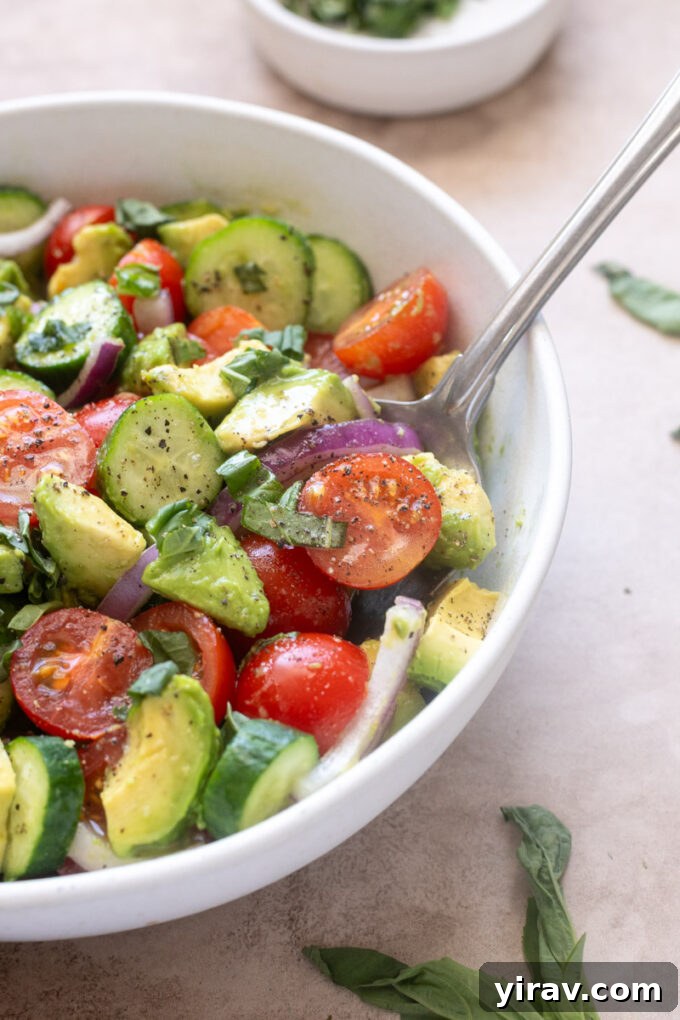 Cucumber tomato avocado salad with lemon vinaigrette in serving bowl with a spoon.