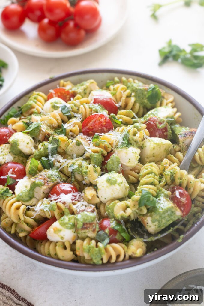 Chicken pesto pasta salad in serving bowl with spoon digging in.
