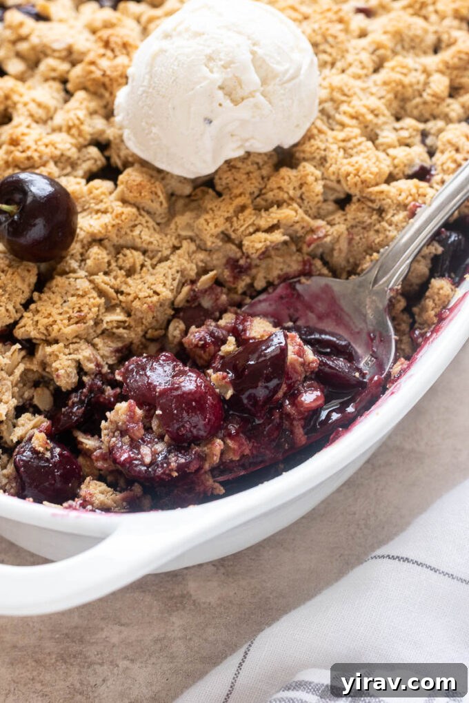Spoonful of fresh cherry crisp in baking dish with ice cream.