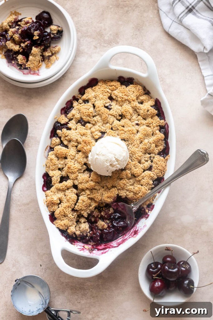 Fresh cherry crisp in baking dish with scoop of ice cream and spoon digging in.
