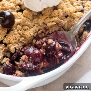 Spoonful of fresh cherry crisp in baking dish with ice cream.