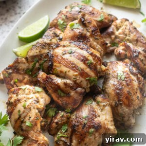 Cilantro-Lime Grilled Chicken with Zesty Marinade 11 Grilled cilantro lime chicken thighs on a white serving platter garnished with fresh cilantro and lime wedges.